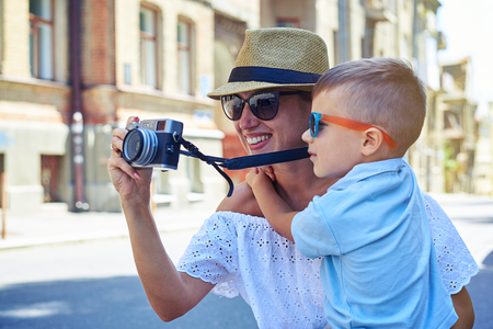 Close-up of young smiling woman with her small son who is taking a photo during their walk in the city on a sunny summer dayの写真素材