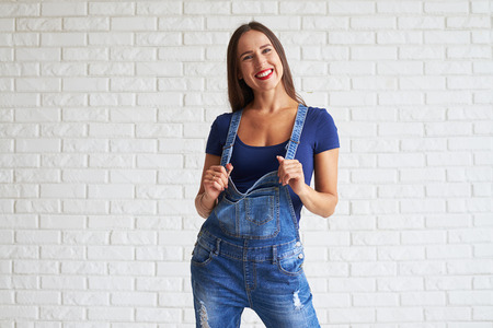 Smiling woman wearing denim suit with blue t-short and standing against a white wallの写真素材