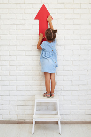 Little girl holds an arrow, standing on a chair, the concept of development and growingの写真素材