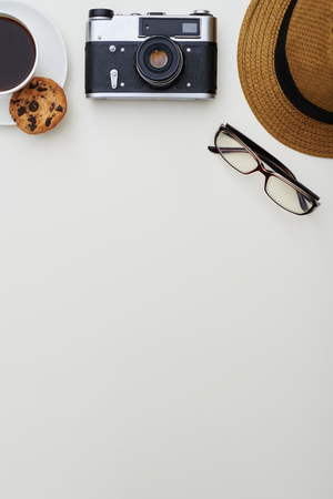 Top view of white surface with hat, eyeglasses, photo camera and a cup of coffee with cookie put on the upper part of itの写真素材