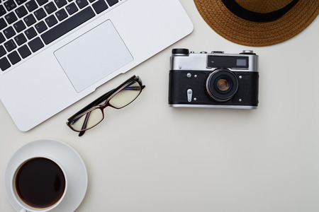 Top view of laptop, eyeglasses, photo camera, hat and a cup of coffee on white surfaceの写真素材