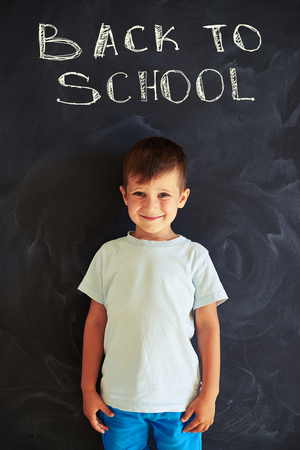Portrait of future first grader standing against school blackboard backgroundの写真素材