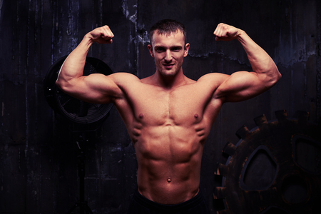 Handsome young bodybuilder is posing shirtless in dim light of the studioの写真素材