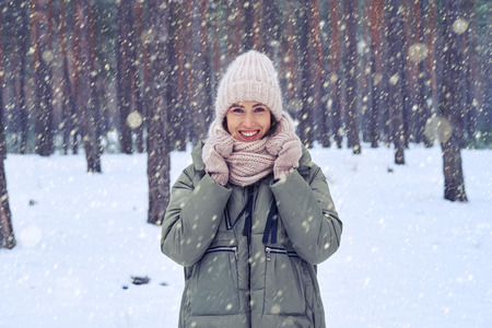 Mid shot of charming young woman in the wintry forest. Wearing pink knitted mittens, cap and scarf...