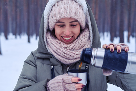 Close-up of female pouring tea from thermos to the cup in a snowy forest. The hand of the woman pouring tea from the thermos in the snowy woodの写真素材