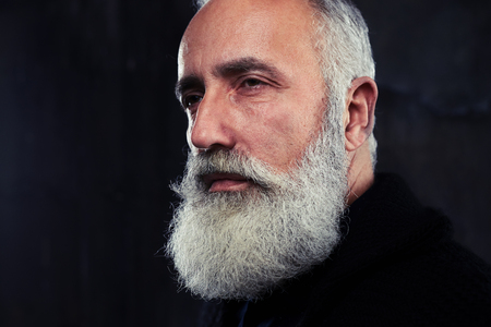 Indoors shot of stylish handsome adult man with gray long gray beard. Man looking aside. The concept of confidence and masculinityの写真素材