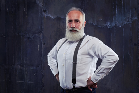 Close-up of attractive Caucasian man standing with hands on hips. Man with gray bead and haircut standing isolated over black backgroundの写真素材