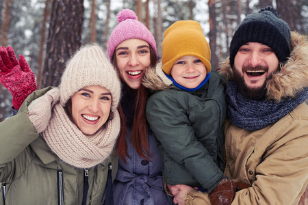 Close-up of overjoyed family hugging during the walk in the forest on vacations. Young Caucasian family spending time together on a cold winter day. The concept of familyの写真素材