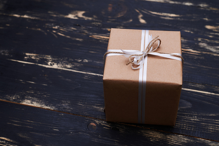 Side view of vintage gift box wrapped with brown paper and tied with rope isolated over shabby wooden backgroundの写真素材