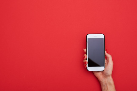 High angle of female hand holding white smart phone blank screen over red background with a copy spaceの写真素材