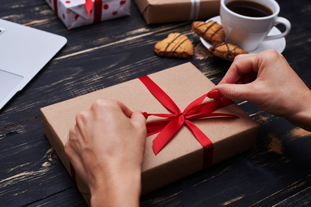 High angle of female hands holding handmade gift box with red ribbon on the shabby wooden backgroundの写真素材