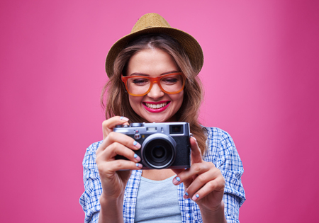 Close-up of cute trendy girl who is looking at the vintage camera isolated over pink background.の写真素材