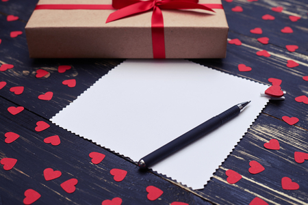 Side view of greeting card for copy space with pen and gift box isolated over flat lay background decorated with small red heartsの写真素材