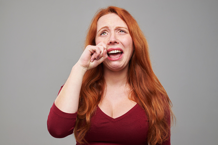 Close-up portrait of Caucasian young redhead woman looking unhappy. Disappointed crying woman wipes tearsの写真素材