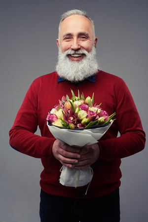 Close-up shot of senior man with a bouquet of different tulips isolated over gray background in the studio. International womens dayの写真素材