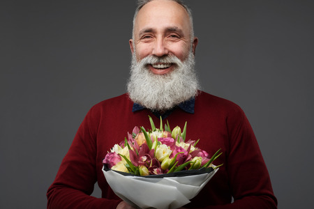 Close-up shot of mature man with a bouquet of different tulips isolated over gray background in the studio. International womens dayの写真素材