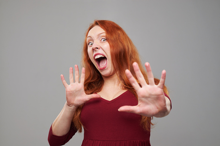 Close-up of redhead young woman isolated over gray background. Holding two hands raised. Protecting from somethingの写真素材