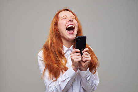 Close-up of merry girl laughing while using telephone. Positive teenager isolated over backgroundの写真素材