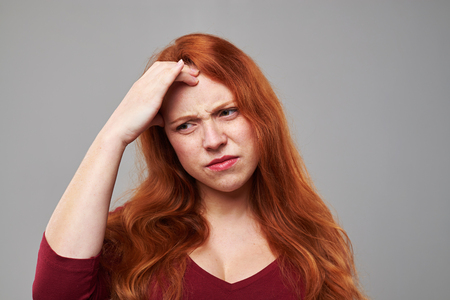 Close-up portrait of young woman having a headache isolated over gray background. Woman feeling bad. The concept of heath careの写真素材