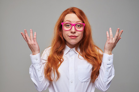 Close-up of frustrated red hair student in pink glasses isolated over background in the studio. Exhausted girl looking tiredの写真素材