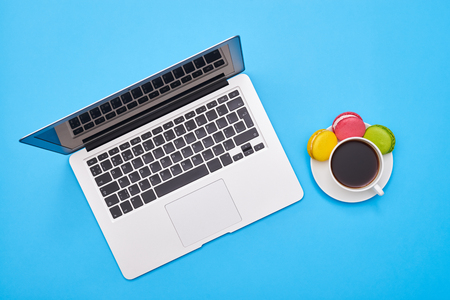Stylish shot of a silver laptop and cup of coffee with colorful macaroonsの写真素材