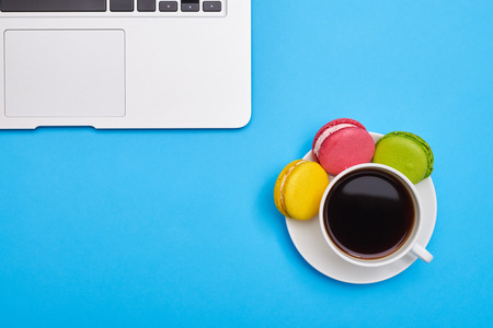 Top view image of a coffee with delicious macaroons and laptop over blue flatlayの写真素材