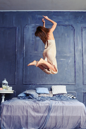 Back view of a female in the air. Woman jumping with knees bent. Wearing long nightgown having fun early in the morningの写真素材