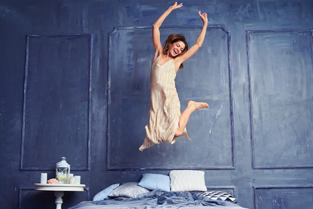 Low angle of a female in the air. Young excited woman jumping on bed. Woman having fun in the bedroomの写真素材