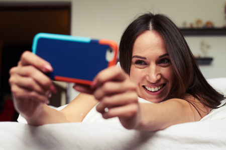 Close-up shot of female making a selfie while lounging on the bed. Enjoying careless morning Rack shot on a telephone.の写真素材