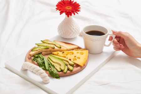 Close-up of bed breakfast with tasty black tea, juicy green avocado and aromatic cheddar for pretty womanの写真素材