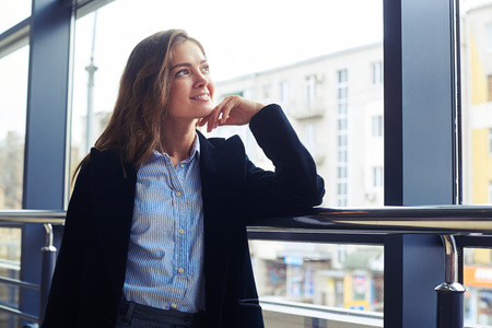 Low angle of romantic woman with loose hair looking through window. Female in formal clothesの写真素材