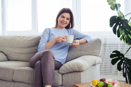 Mid shot of pretty woman having rest on sofa with cup of coffee