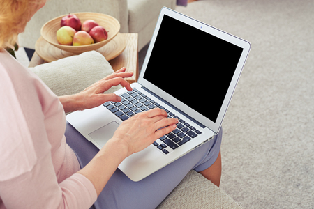 Cropped shot of woman working in laptop while sitting on cozy sofa in bright living roomの写真素材