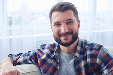 Close-up of smiling bearded mister leaning on back oh sofa and having rest