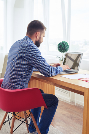 Vertical of stylish gentleman in blue checkered shirt working with laptopの写真素材