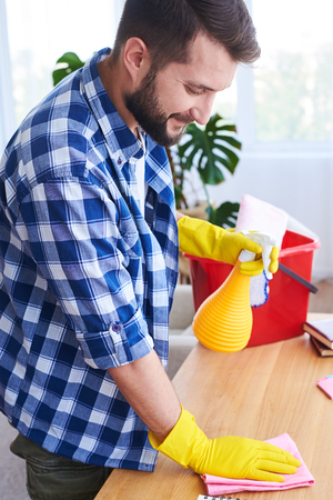 Vertical of caring guy pulverizing and dusting working place in bright roomの写真素材