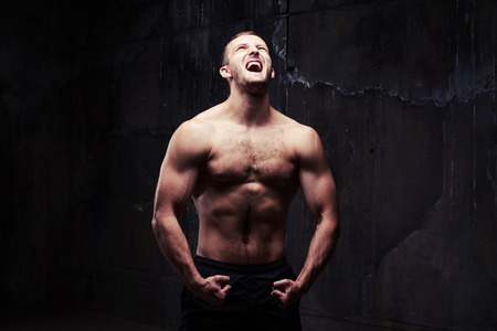 Close-up shot of angry man screaming while holding wrists together showing his pumped musclesの写真素材