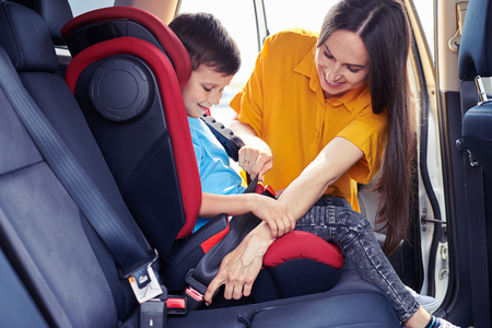 Wide shot of gorgeous mom helping son sitting in baby seat to fasten seat belt