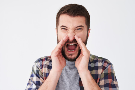 Close-up shot of angry bearded man shouting loudly with hands on the mouth. Emotion, advertisement and people conceptの写真素材