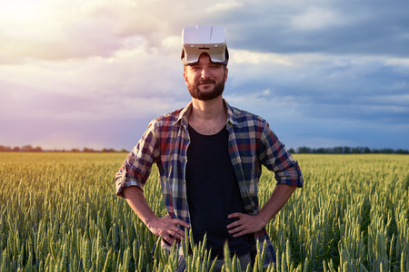 Young bearded man standing on field of weed wearing 3D glasses on head, looking in camera, mid shotの写真素材