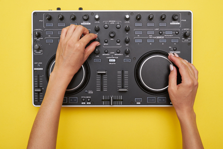 Flat lay of mixing board on yellow background. View of hands of woman using electronic device, mid...
