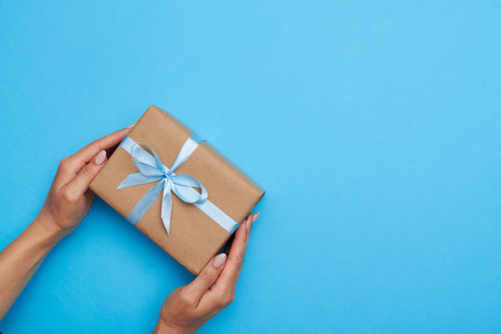Top view of hands placing a wrapped box, tied with a ribbon. Gift box lying on blue backgroundの写真素材