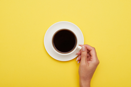 Flat lay of girl hand holding cup of tasty espresso with copy space on yellow backgroundの写真素材