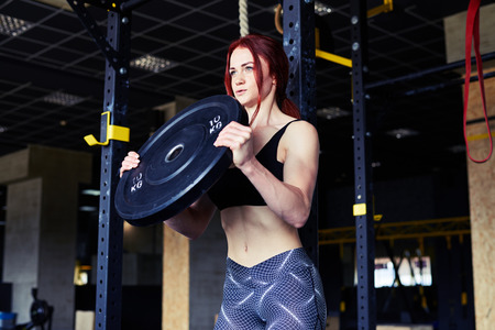 Close-up shot of attractive girl working out with barbell in gym. Pumping up muscles