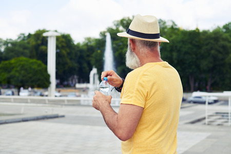 Rear view of man in straw hat holding plastic bottle of water with urban cityscapeの写真素材