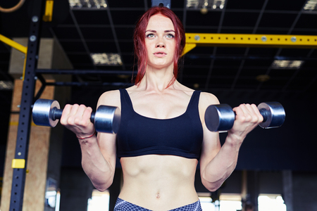 Low angle of sporty girl showing her well trained body. Fitness woman with lifting dumbbellsの写真素材