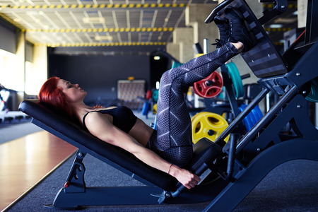 Side view of young woman working her quads at machine press in the gymの写真素材