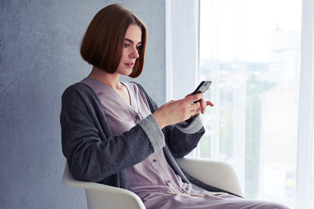 Mid shot of beautiful young woman using telephone and sitting on armchair with copy space