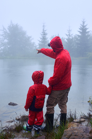 Rear view of father showing something to son on lake. Morning on Carpathian mountainsの写真素材