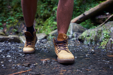 Close-up of boots of hiker man crossing mountain riverの写真素材